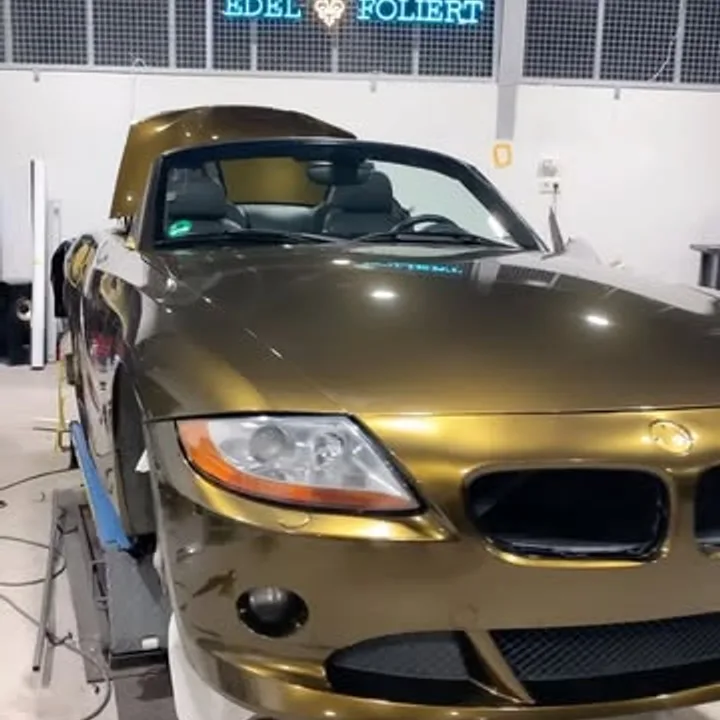 BMW Z4 in Gold-Chrom foliert unter dem beleuchteten Edelfoliert-Schriftzug in der Werkstatt