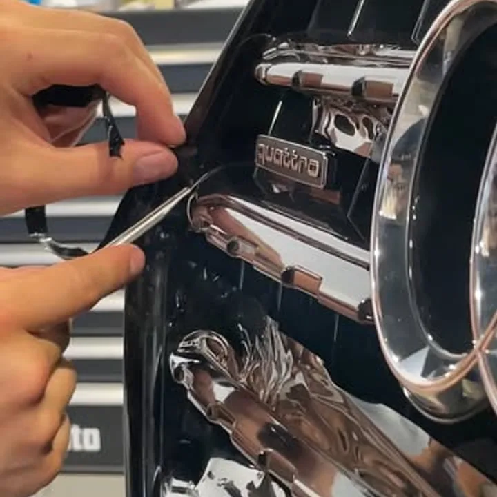 Hände lösen die Chromleiste am Kühlergrill eines Audi quattro für ein Chrome Delete