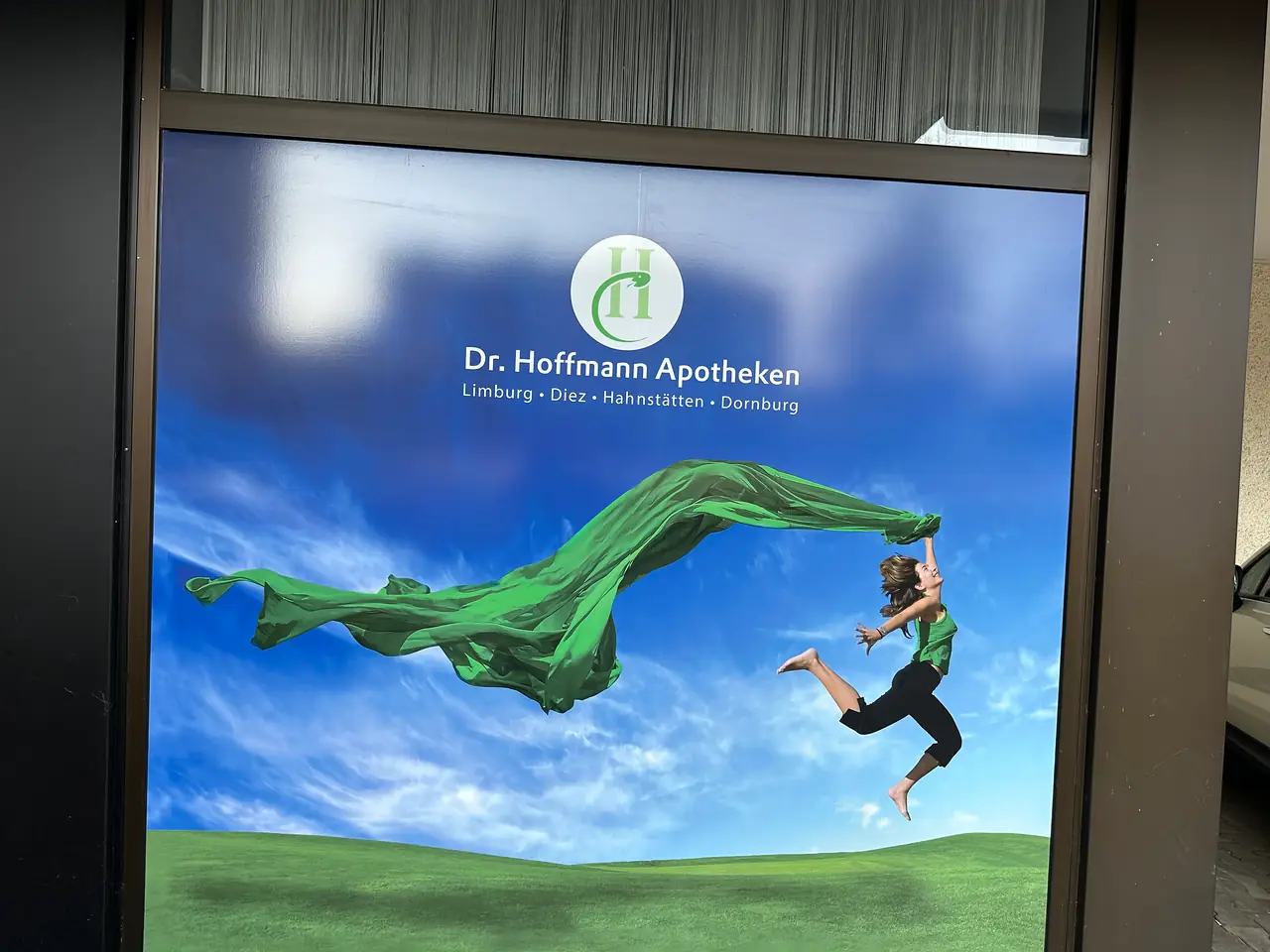 Schaufenster vollflächig foliert: Logo und springende Frau mit grünem Tuch